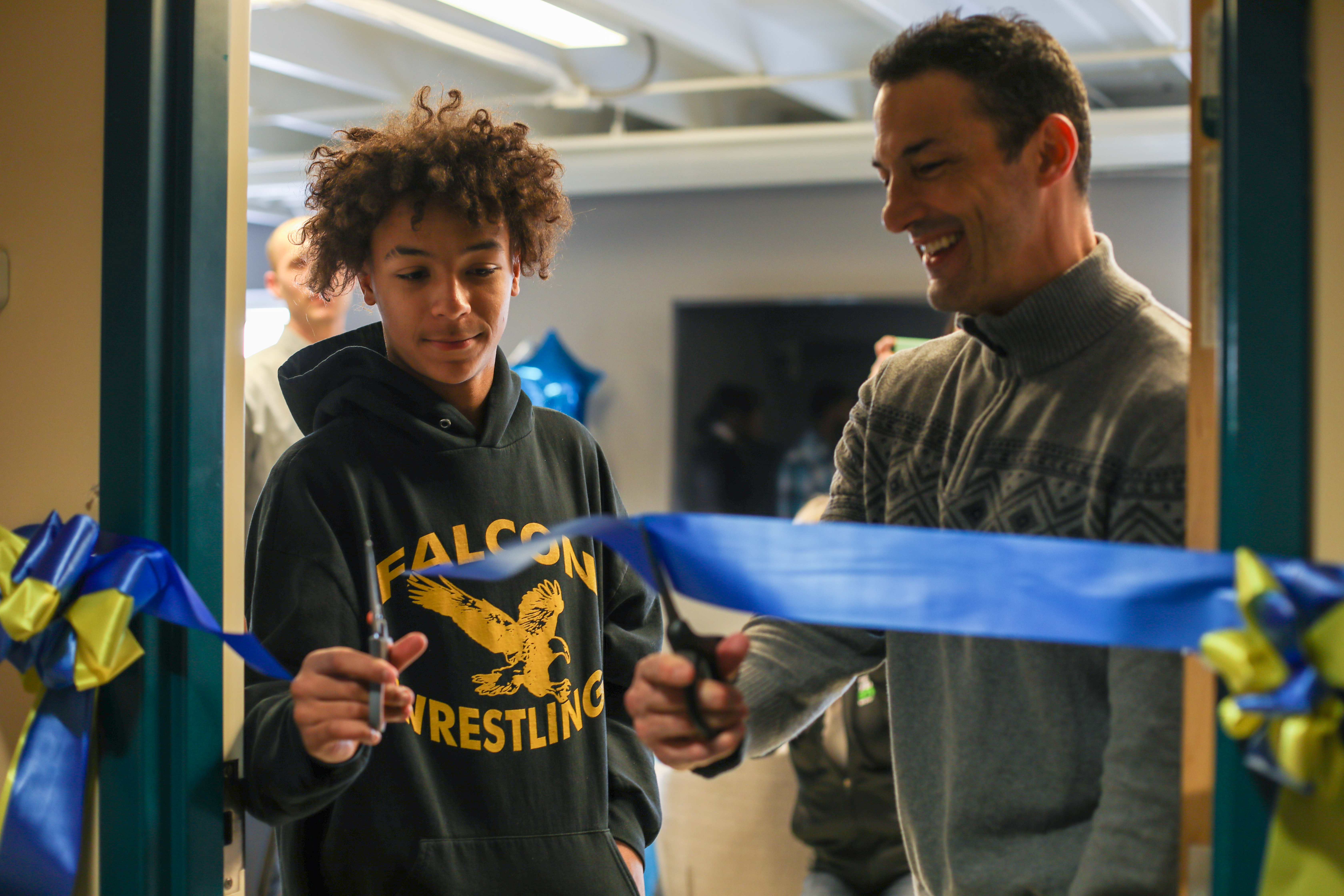 The blue ribbon was cut in a ceremony by a local teen boy accompanied by an adult while standing in the doorway to the new room.