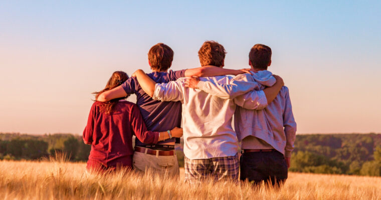 A team of young adults sitting on a grain field watching a lovely sunset