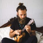 Man with beard playing ukulele.