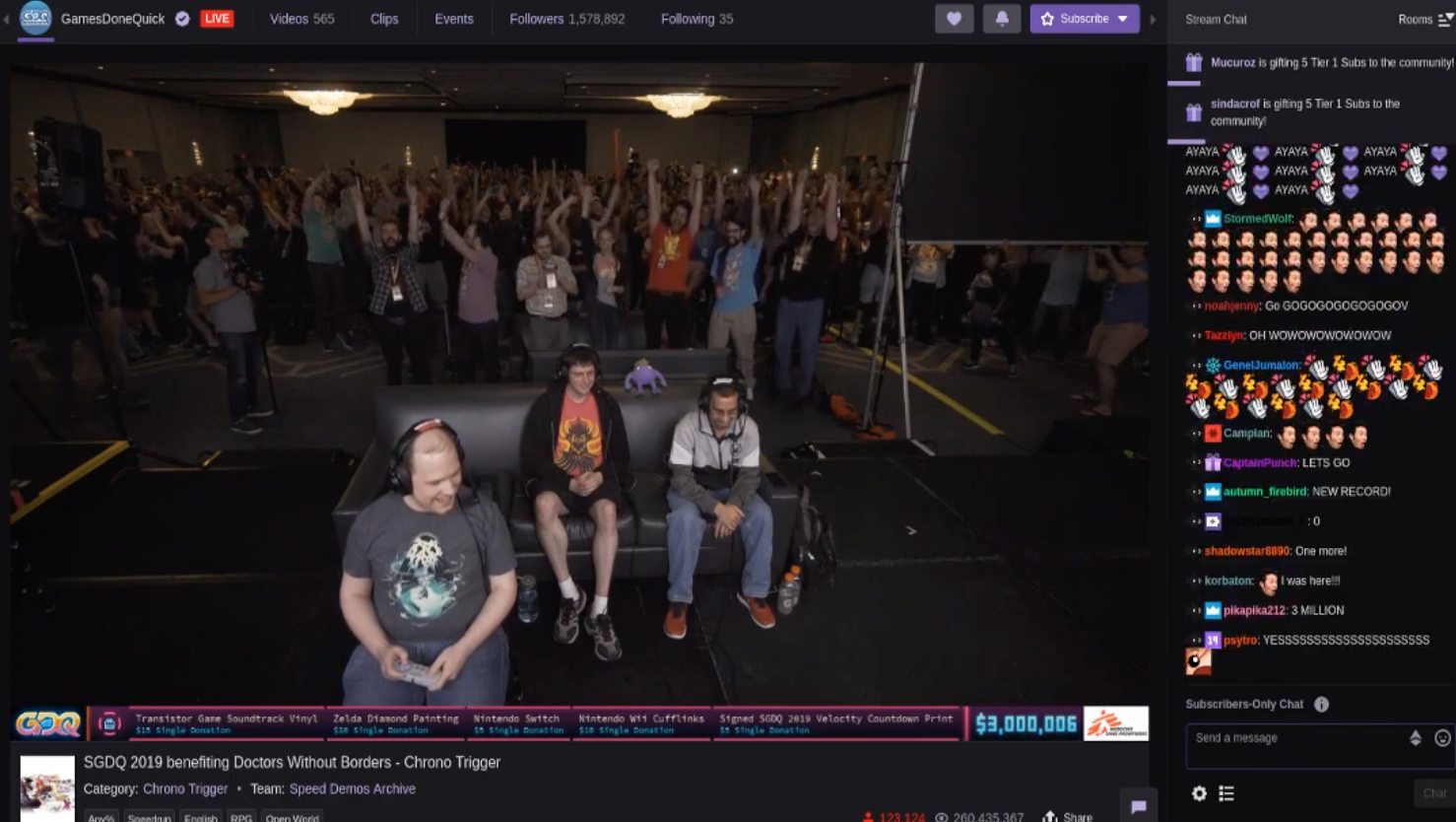 A screenshot of a gaming marathon shows a crowd of people watching behind gamers playing as well as a stream of online comments. 