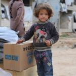Child standing in front of a UNHCR supply box.