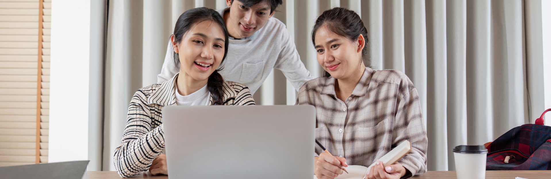 A small team of nonprofit workers smiles while reviewing information on a laptop together, suggesting teamwork, collaboration, and planning.
